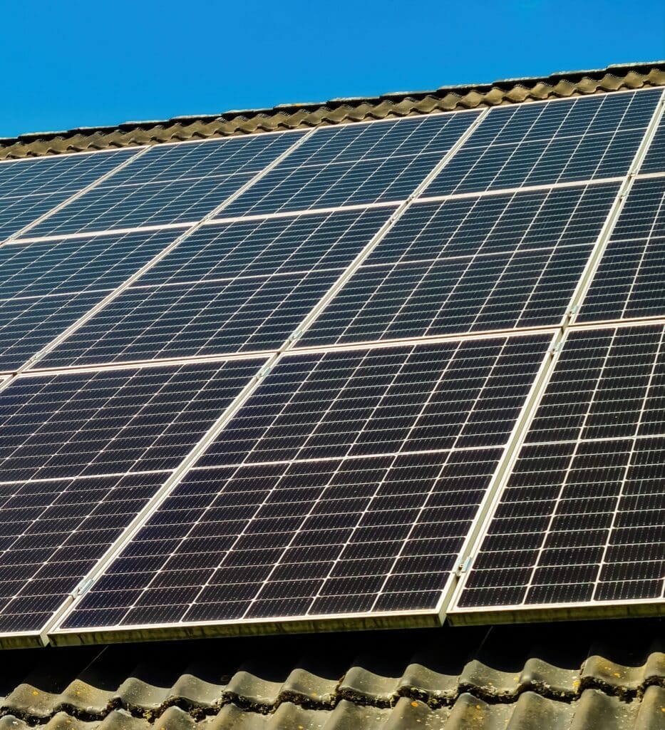 Panneaux Solaires sur Toit: Énergie Propre et Durable Panneaux solaires sombres sur un toit en tuiles foncées, partiellement couvert de mousse, sous un ciel bleu clair.