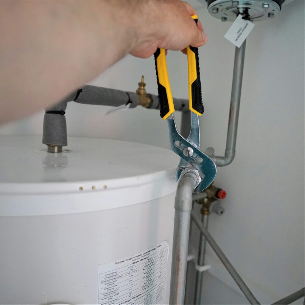 Réparation chauffe-eau ThermaQ: Guide pince plombier Main serrant un raccord de tuyau de chauffe-eau ThermaQ Evocyl 180 avec une pince de plombier jaune et noire. Installation ou maintenance.